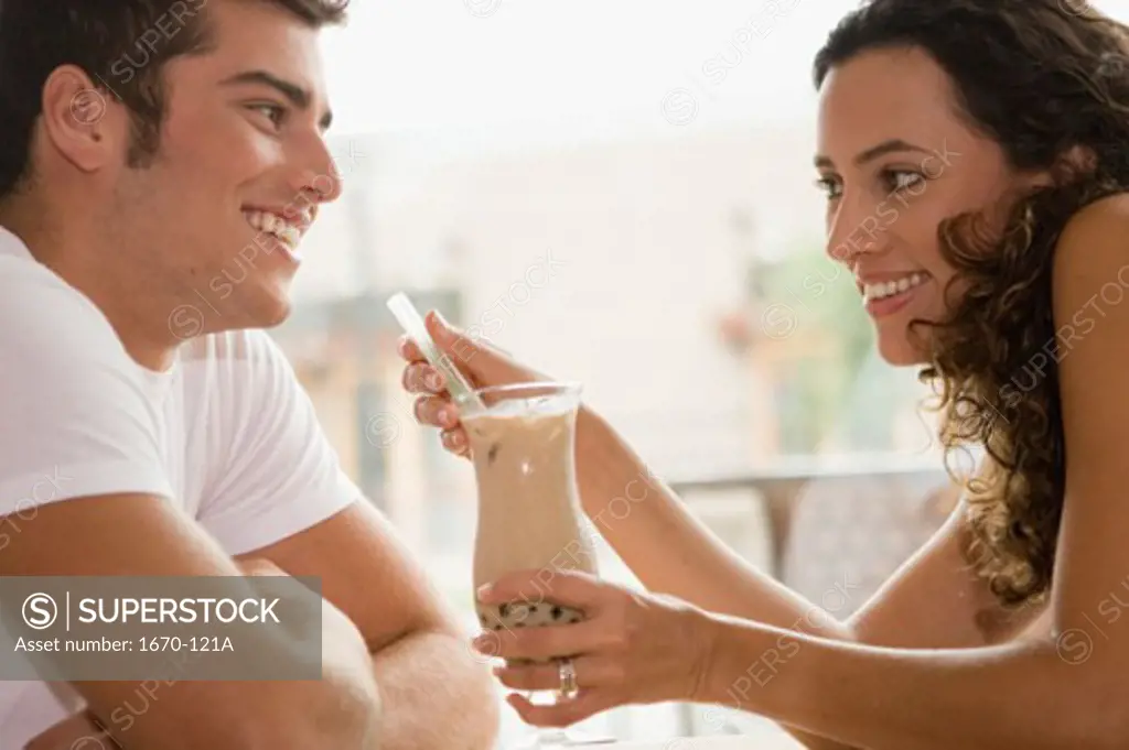 Side profile of a young woman holding a milkshake with a teenage boy sitting in front of her