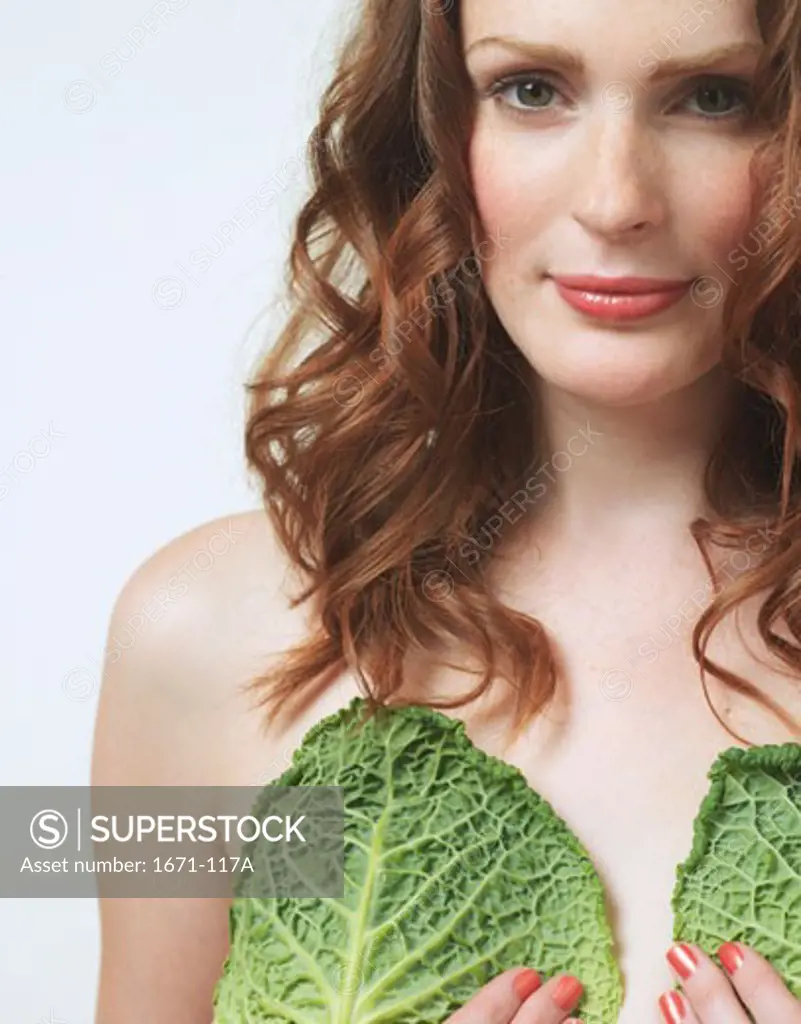 Close-up of a young woman holding savoy cabbage leaves on her chest