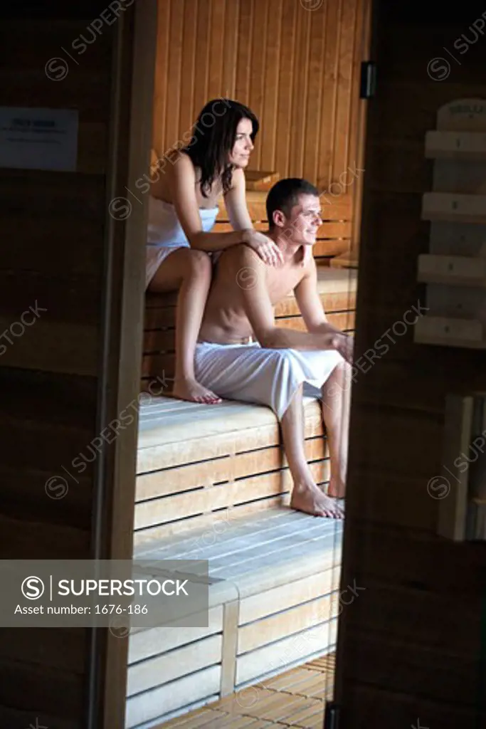 Young woman sitting behind a young man in a sauna