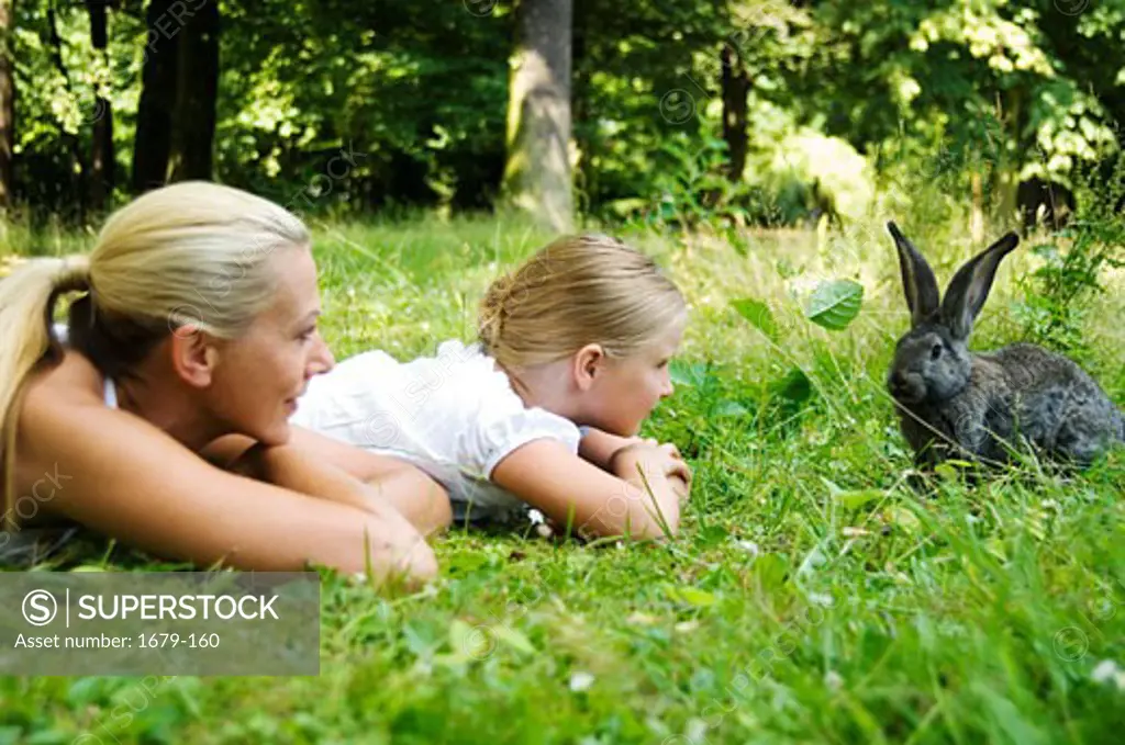 Mid adult woman and her daughter playing with a rabbit in a park