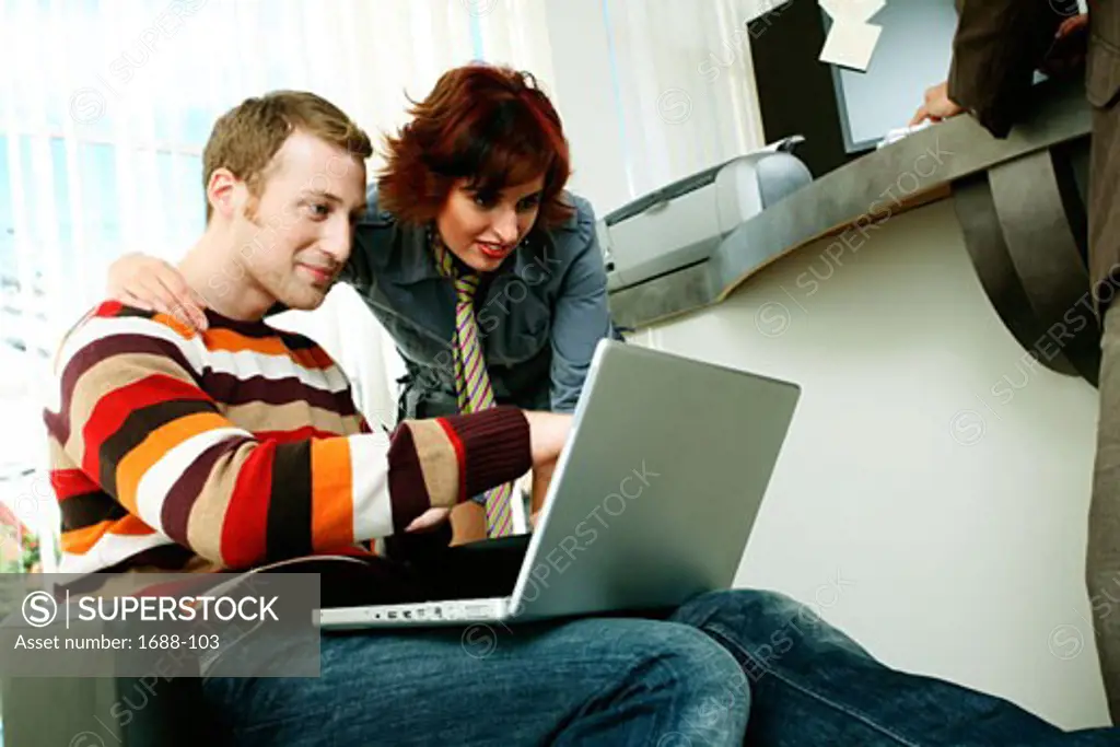 Businessman using a laptop with a businesswoman standing beside him