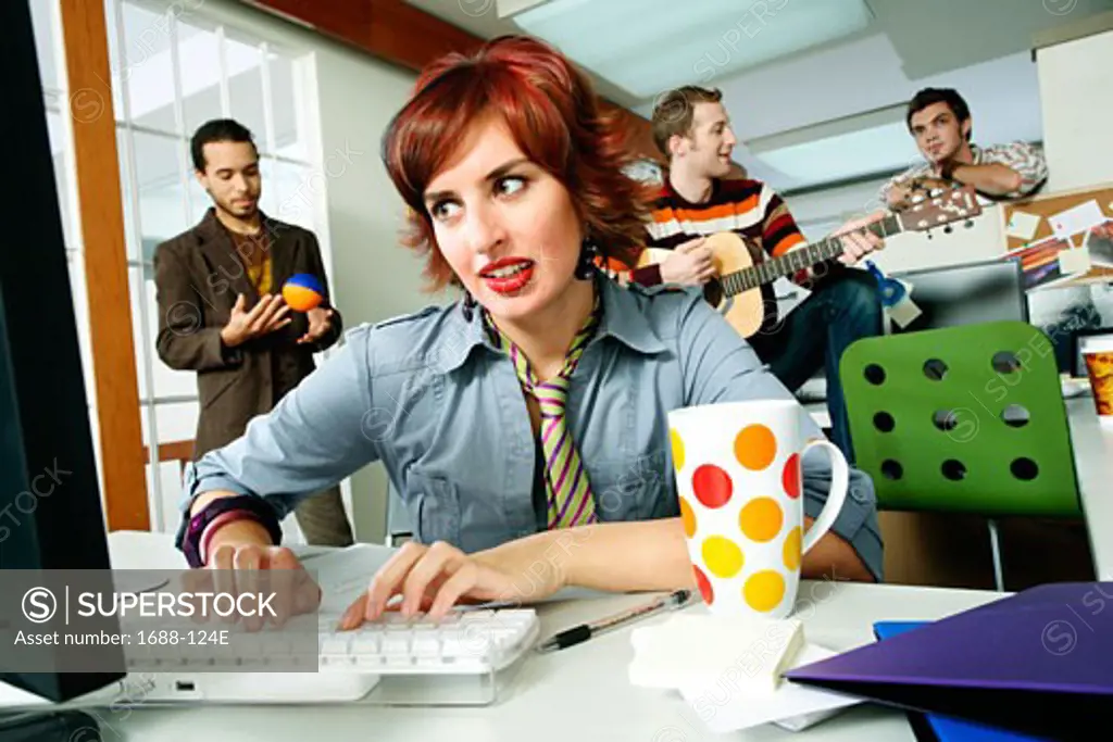 Businesswoman using a computer with three businessmen playing behind her