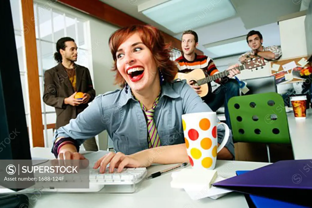 Businesswoman using a computer and laughing with three businessmen playing behind her