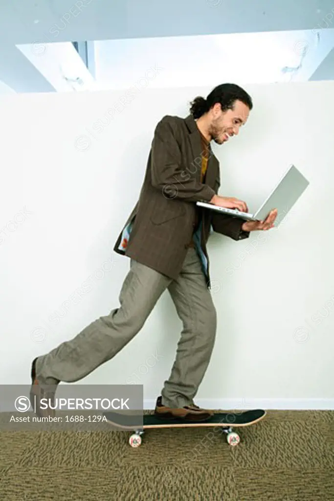 Businessman riding a skateboard and using a laptop
