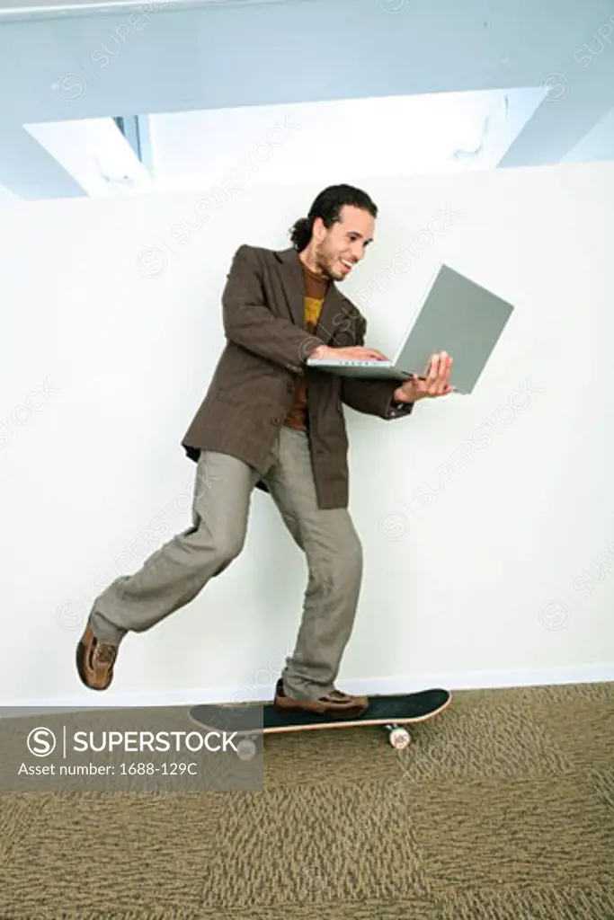 Businessman riding a skateboard and using a laptop