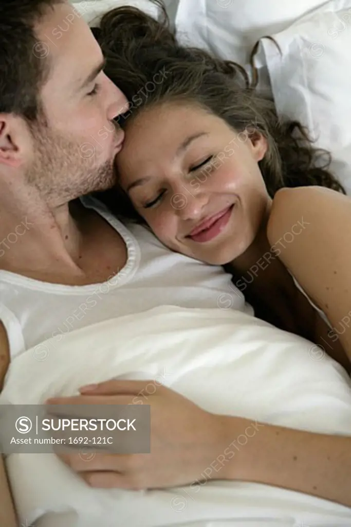 Young man kissing a young woman's forehead in bed