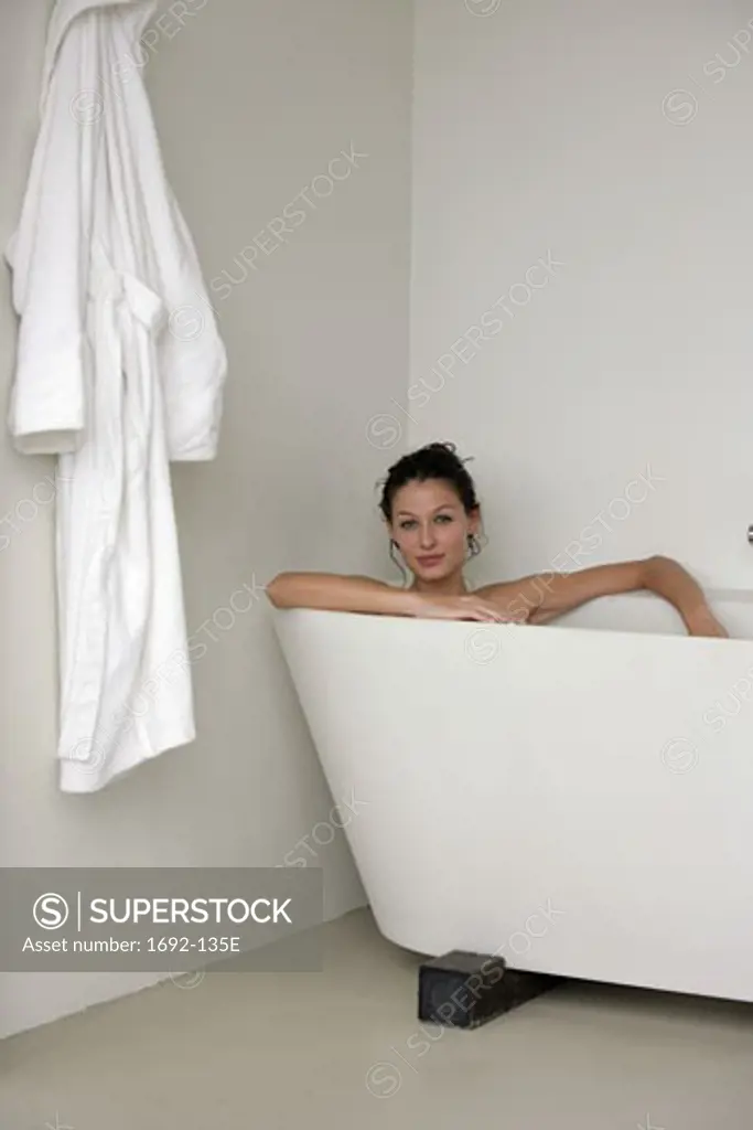 Portrait of a young woman in a bathtub with a bathrobe hanging on the wall