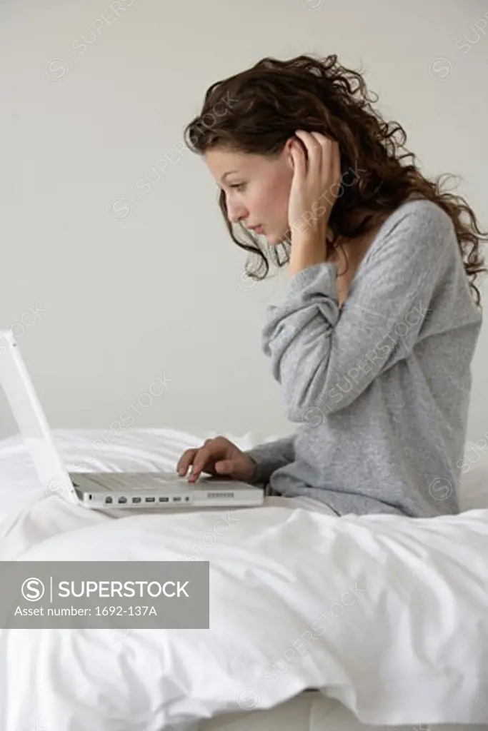Young woman sitting in bed and using a laptop