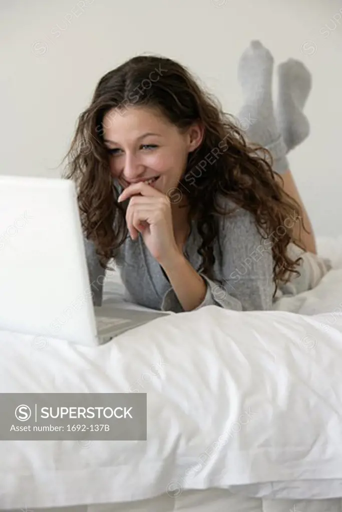 Young woman lying in bed and using a laptop