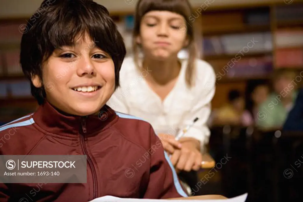 Portrait of a boy in a classroom with a girl looking over his shoulder