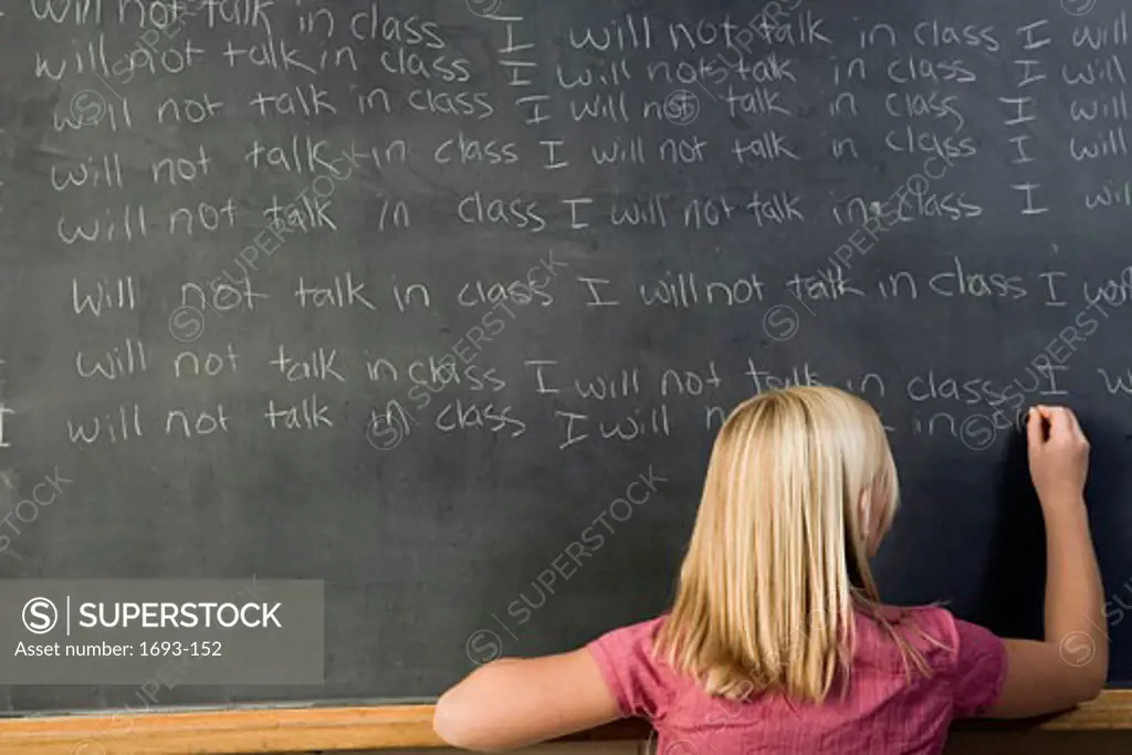 Rear view of a girl writing on a chalkboard