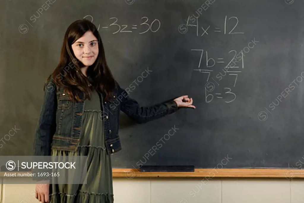 Girl standing in front of a chalkboard pointing to a math problem
