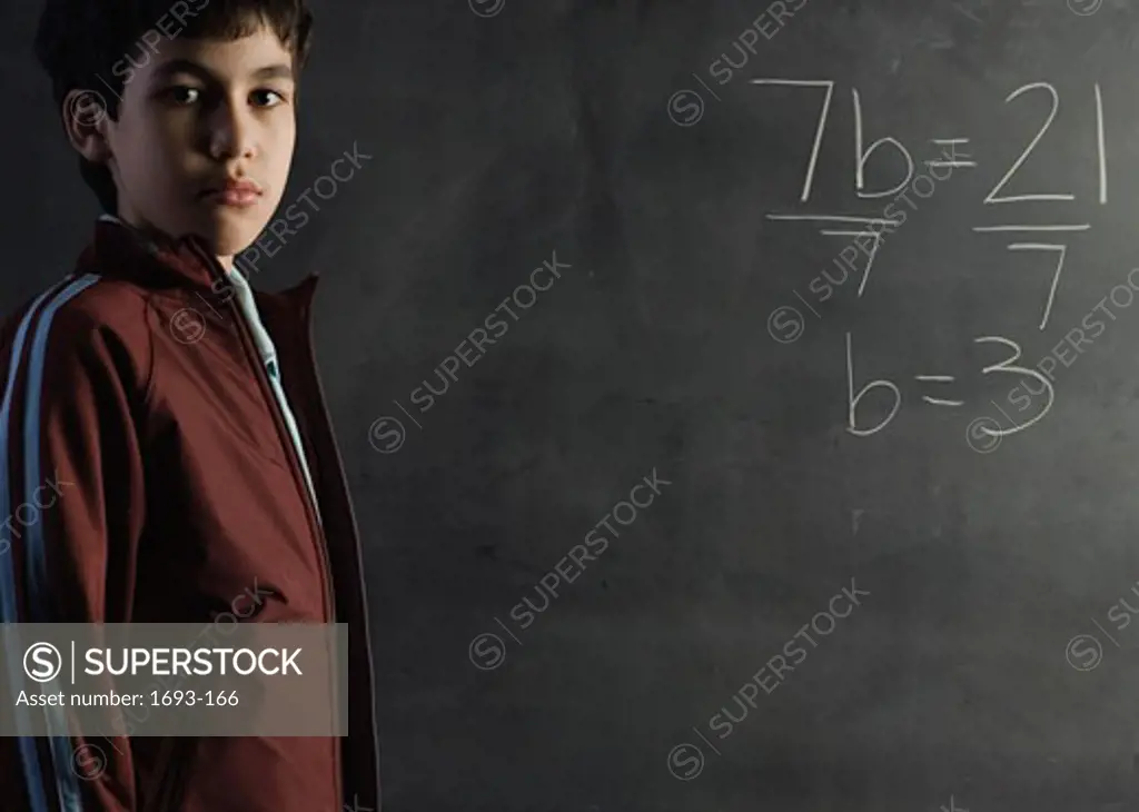 Boy standing in front of a chalkboard near a math problem