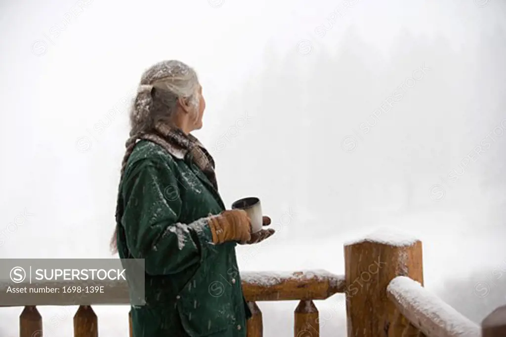 Senior woman standing by a railing and holding a coffee cup