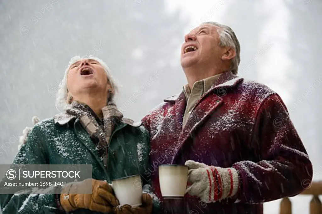 Senior couple holding coffee cups and looking up with their mouths open