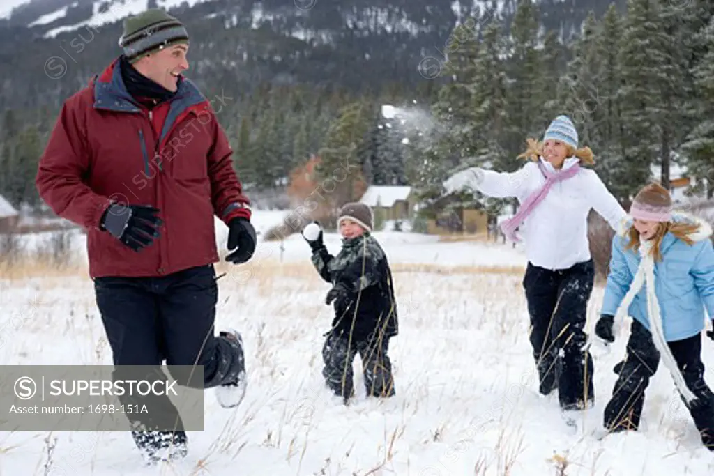 Mature woman with her son and daughter throwing snowballs at a mature man