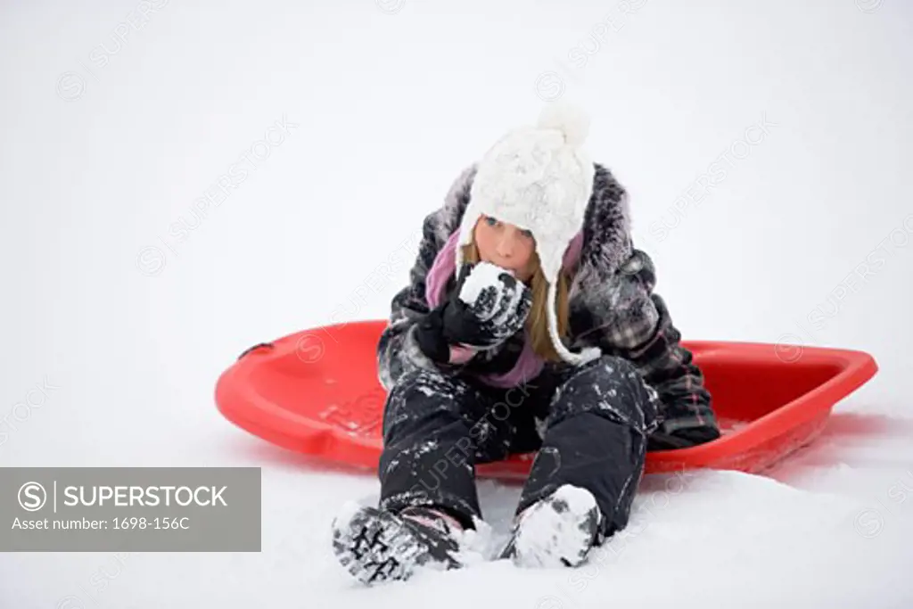 Girl sitting on a sled and eating snow
