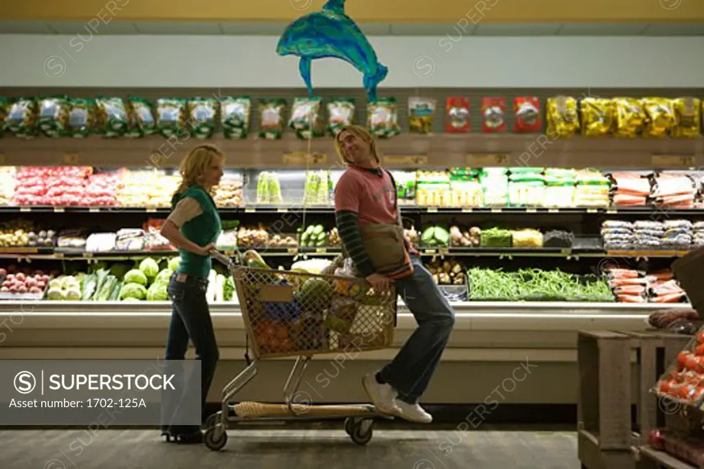 Young woman pushing a young man on a shopping cart in a supermarket