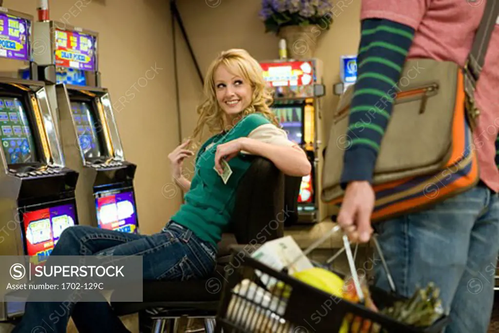 Man carrying a shopping basket with a young woman sitting behind him in a casino