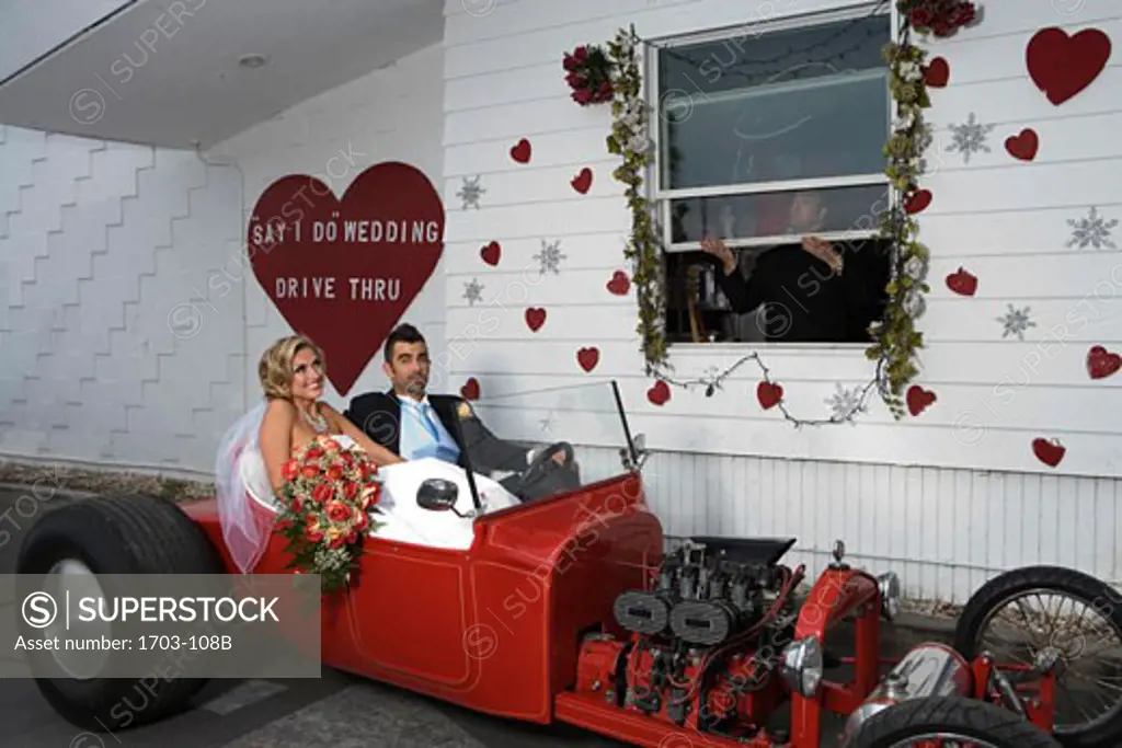 Bride and groom sitting in a convertible car at a drive-thru wedding chapel