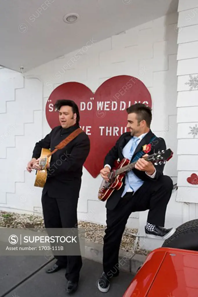 Two men playing guitars in front of a sign