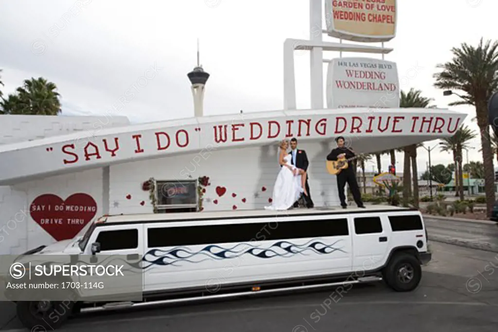 Bride and groom standing on a limousine with a mature man at a drive-thru wedding chapel