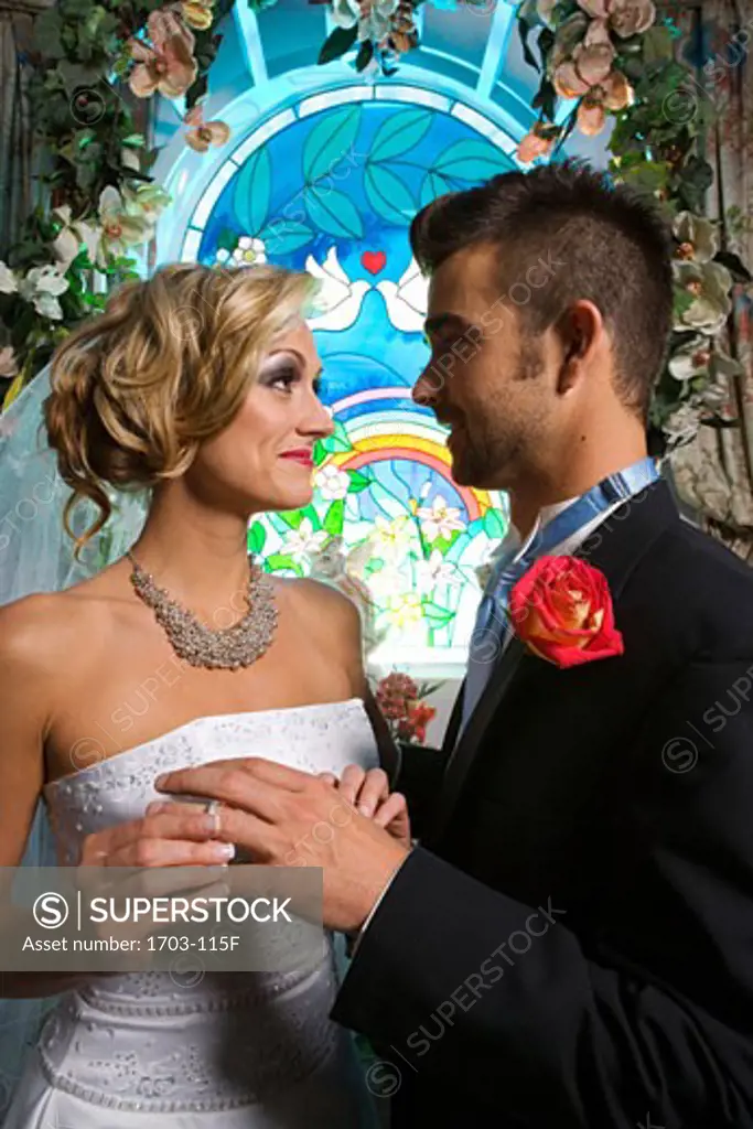 Bride putting a ring on a groom's finger in front of a stained glass window