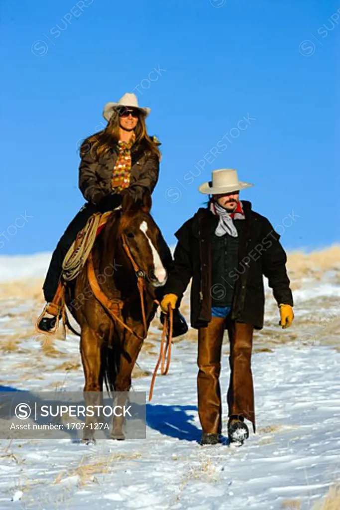 Mid adult woman riding a horse with a mid adult man guiding them