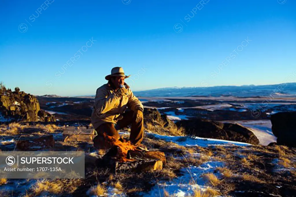Mature man kneeling in front of a campfire