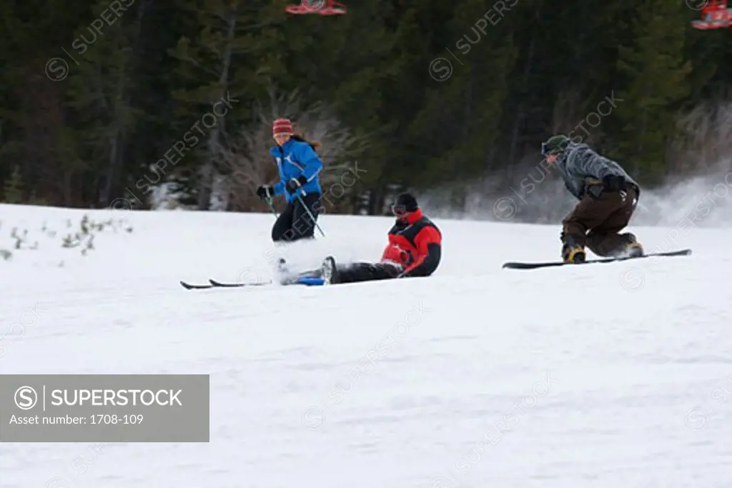 Young woman skiing with mid adult men snowboarding and sledding