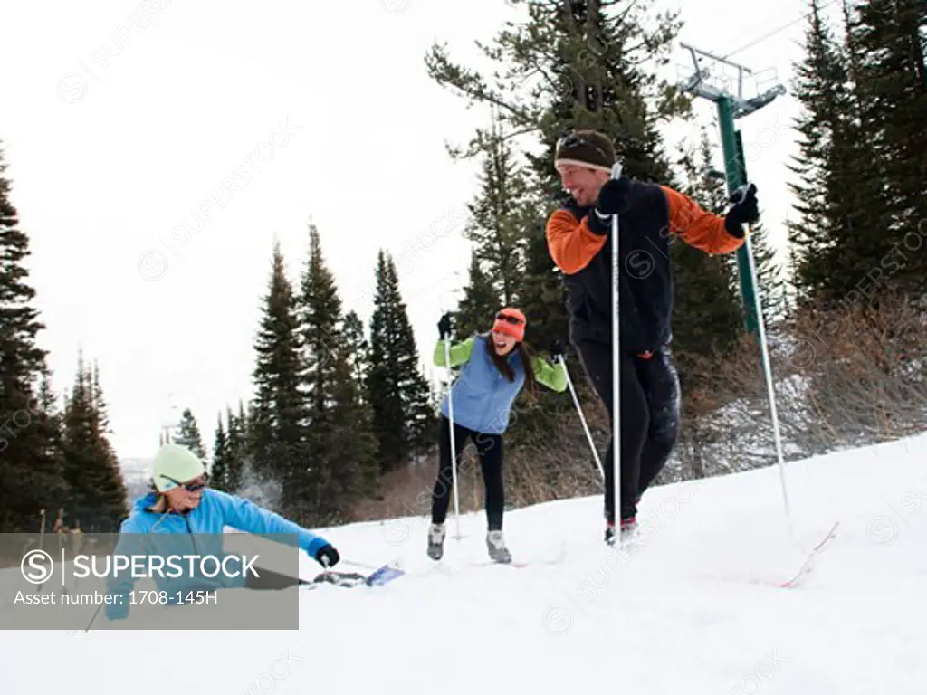 Two people skiing and one person falling