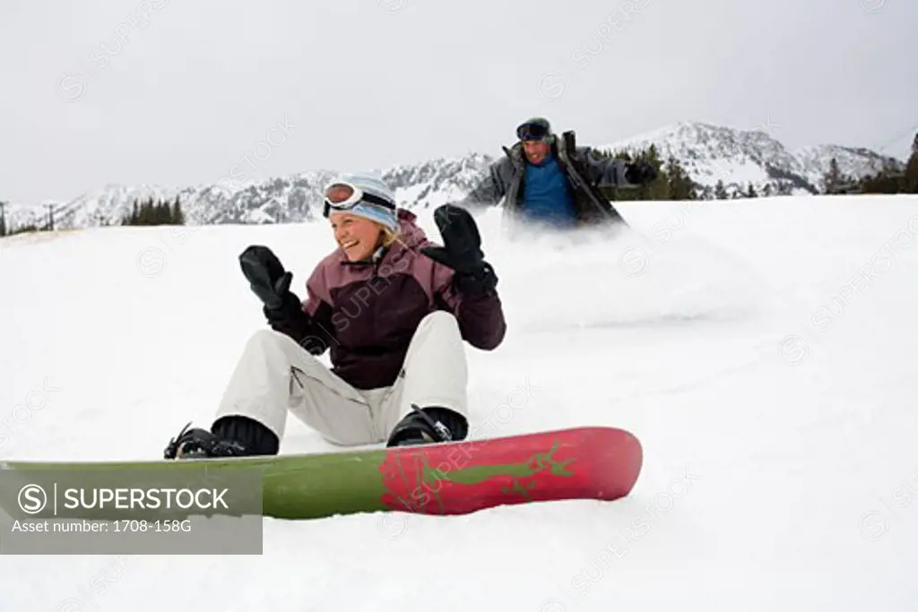 Mid adult woman sitting on snow with a mid adult man sliding behind her