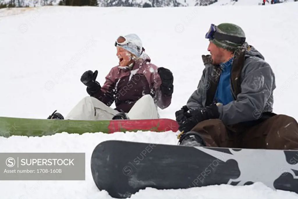 Mid adult couple sitting on snow with snowboards