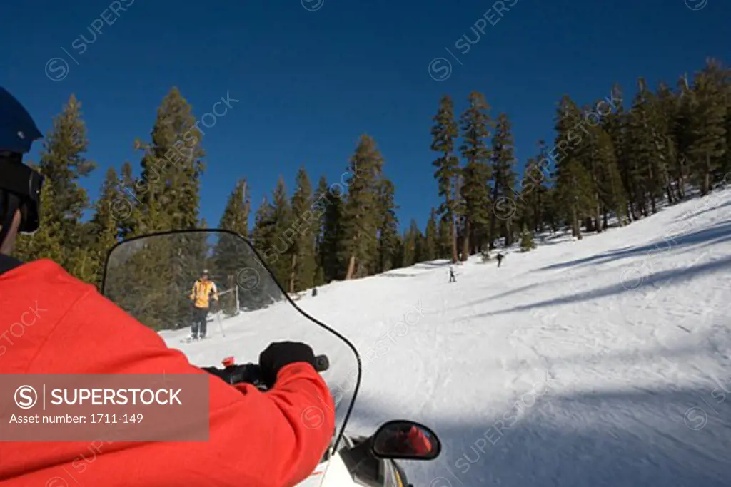 Three people skiing downhill with another person riding a snowmobile
