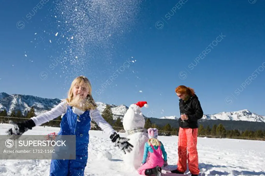 Girl throwing snow with her mother and sister in the background
