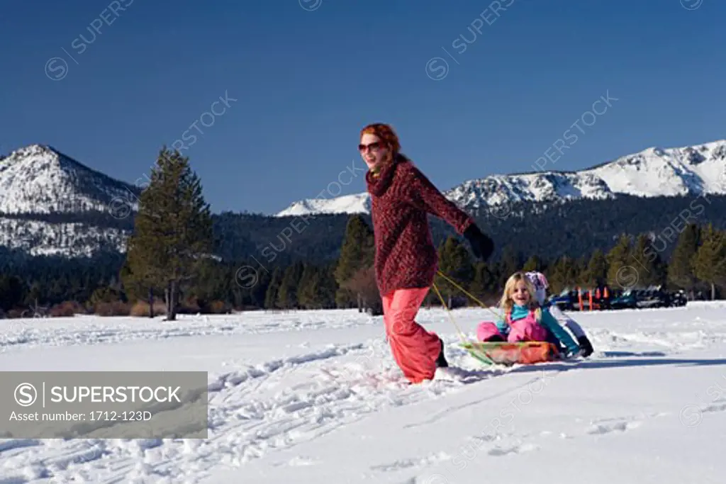 Mature woman pulling her daughters on a sled