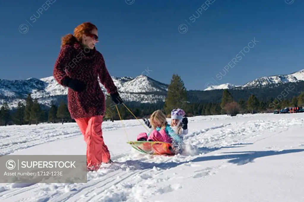 Mature woman pulling her daughters on a sled