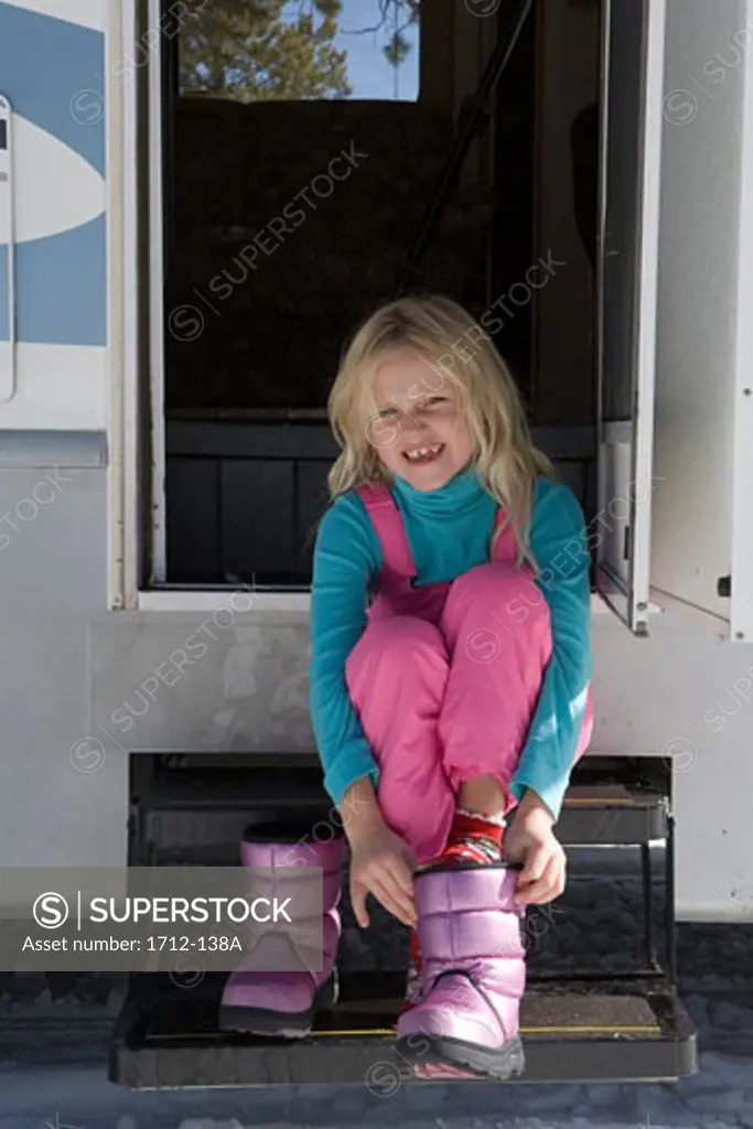 Girl sitting on the steps of a recreational vehicle and putting on her boots
