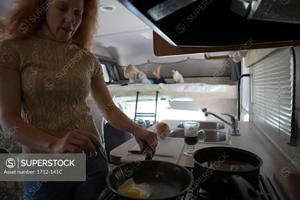 Mature woman cooking in a recreational vehicle with her daughter in the background