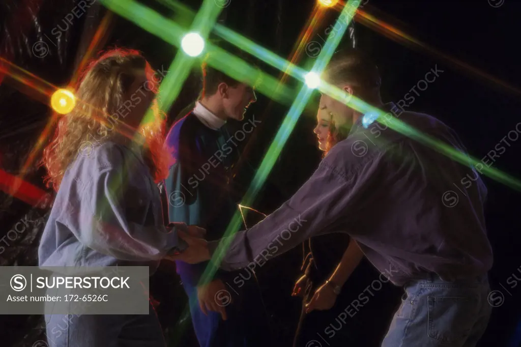 Side profile of a teenage couple and a young couple dancing together in a nightclub
