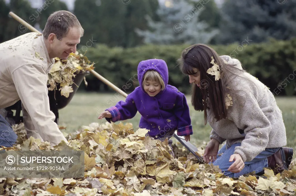 Parents and their daughter raking a lawn