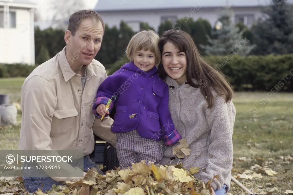 Portrait of parents and their daughter near pile of leaves