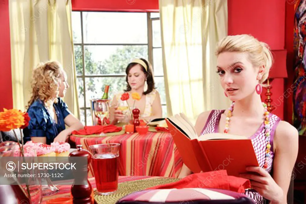 Young woman holding a book with two young women dining in a resturant behind her