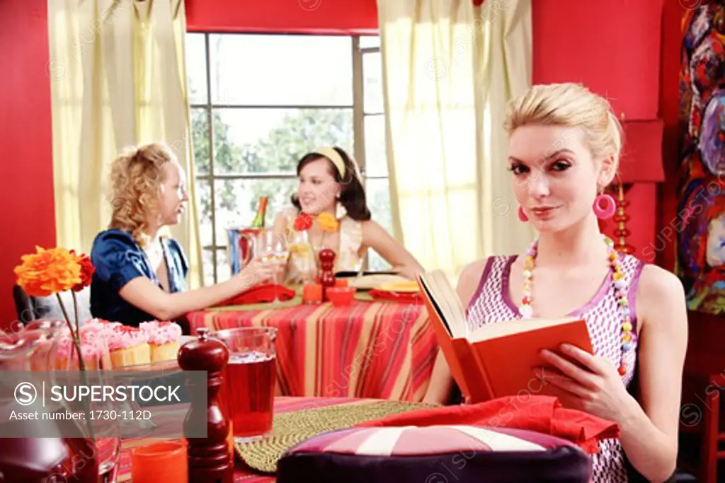 Young woman holding a book with two young women dining in a resturant behind her