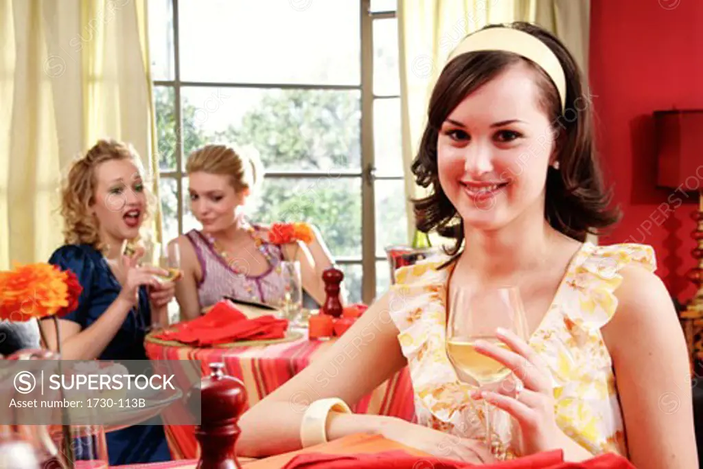Young woman holding a wineglass with two young women dining in a restaurant behind her