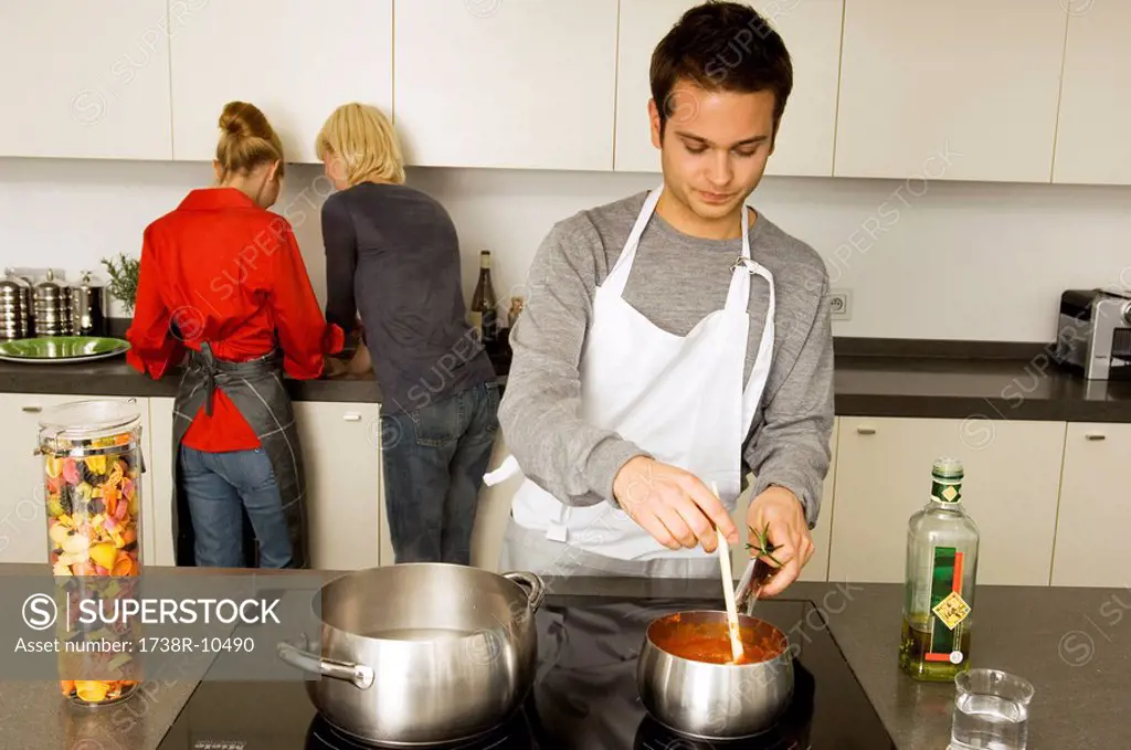 Young man cooking food with two young women standing behind him