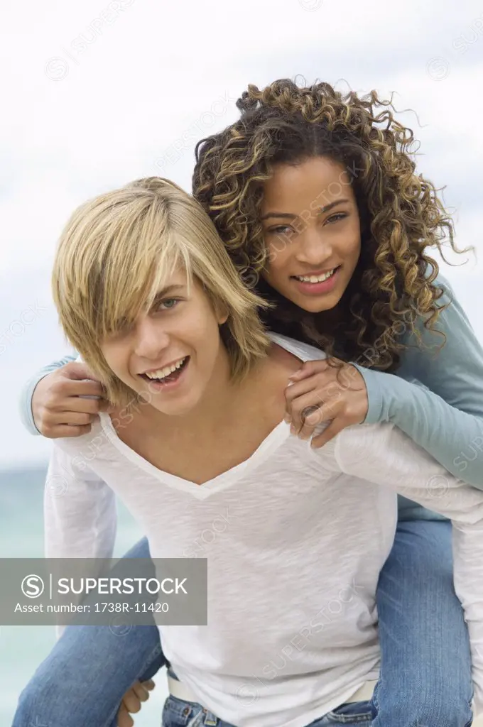 Girl riding piggyback on a teenage boy on the beach