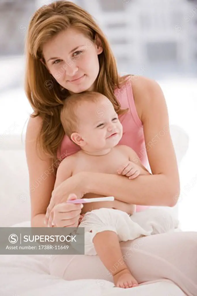 Woman holding a pregnancy test stick with her daughter sitting on her lap