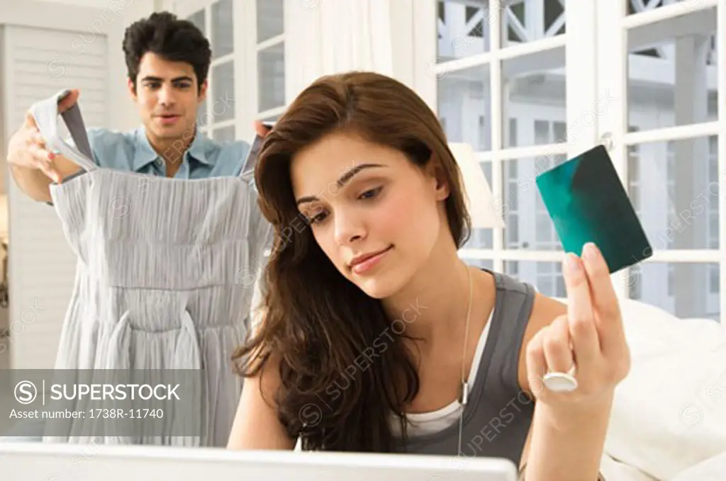 Woman shopping online with a credit card and her husband showing a dress