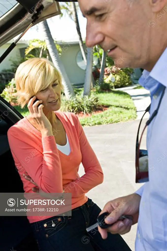 Man holding a car key beside a woman talking on a mobile phone